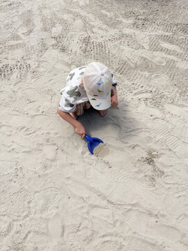 Child digging with blue shovel in playground sand