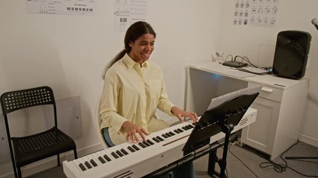 African American teenager playing digital piano in music studio, smiling and talking during lesson. Ideal for promoting music education, creative hobbies, and online learning platforms
