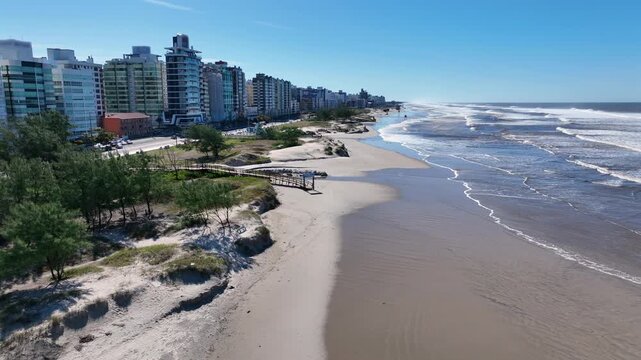 Cap&atilde;o da Canoa beachfront forward push over sandy dunes with ocean and mid-rise buildings