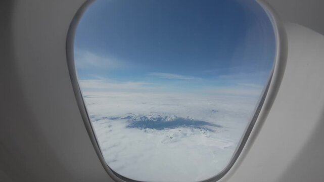 Stunning aerial view of clouds and snowy mountains from the porthole of a jumbo jet in flight