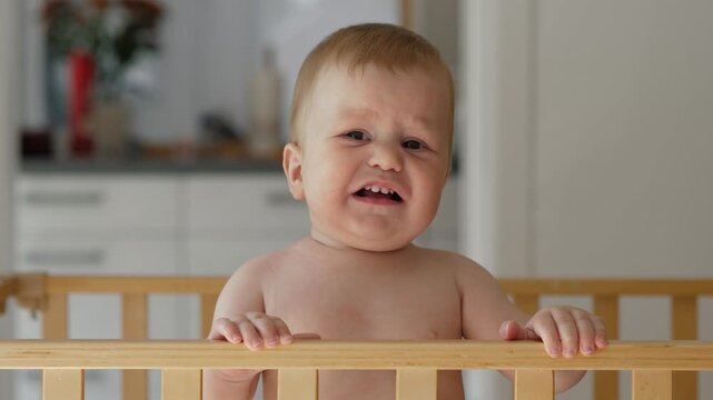 The baby peers over the edge of the crib, displaying a variety of facial expressions, from curiosity to pity, in the cozy and welcoming atmosphere of the home