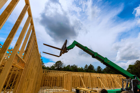 Construction workers use lift to assemble wooden trusses frames at building site