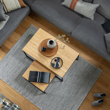 Overhead view of a modern living room with a modular gray sofa, contemporary wooden coffee tables, and a grey rug