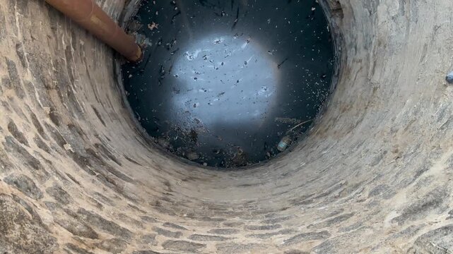 View inside the historic othman well in madina, featuring deep water and stone ruins.