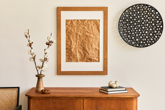 Stylish neutral living room interior with mock up poster frame, cotton flowers, and home decor on wooden commode