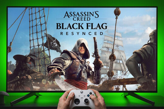 Assassin's Creed Black Flag Resynced Key Art Displayed on TV Screen with Xbox Controller Held in Hands