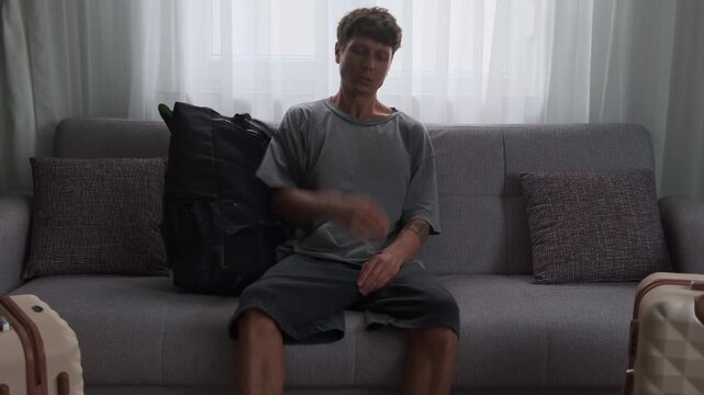 Relocation fatigue and moving stress. Man arriving at temporary apartment with luggage and backpack, exhausted after transition and travel