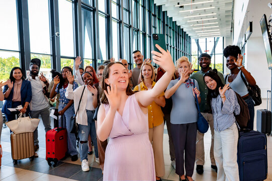 Diverse group of friends taking airport selfie waving goodbye
