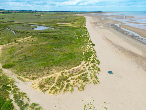 Drone view of an empty North Norfolk, UK beach apart from a single person blue tent seen near to top of the beach. In the distance is the seaside town of Hunstanton. To the left salt marshes.