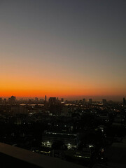 Obraz premium Vibrant sunset over the city skyline at twilight with illuminated urban buildings