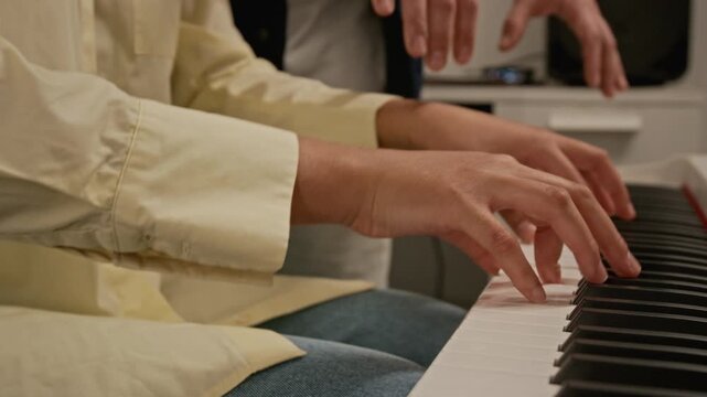 Close-up shot of hands of unknown female student playing digital piano while male instructor guiding her hands during music lesson. Clip for promoting private tutoring and creative education programs