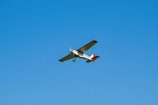 Small propeller plane flies in clear blue sky. The aircraft has white and red accents on wings and tail. The single-engine plane travels through air on sunny day, ready for journey.