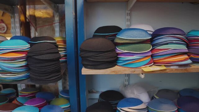 Colorful stacks of traditional Jewish religious head coverings, known as kippot or yarmulkes, displayed for sale on shelves in a store or market, symbolizing faith and cultural identity