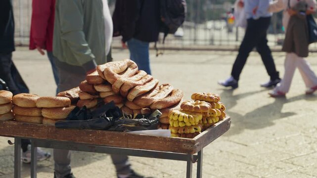 A street food stall in Old City of Jerusalem selling various types of fresh traditional bread and Jerusalem bagels, with crowd of people walking in the background on a sunny day in busy city square