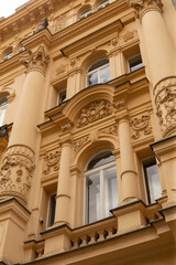 Obraz premium Upward view of a pale yellow historic building facade featuring tall classical columns, arched windows, ornate stucco reliefs and balustrades. Soft daylight