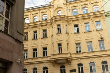 Obraz premium Facade of an ornate pale yellow historic apartment building showcasing decorative stucco, window cornices, arched ground-floor openings, small balconies