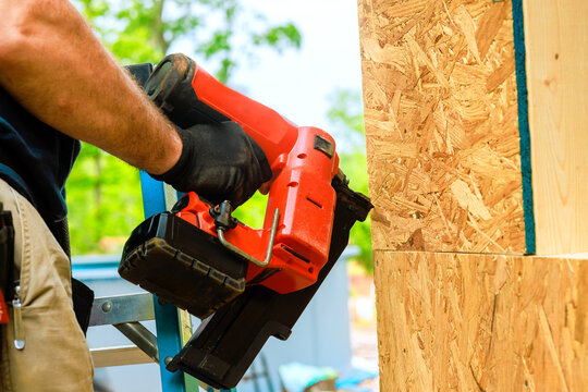 Worker uses nail gun to fasten wood panels at construction site