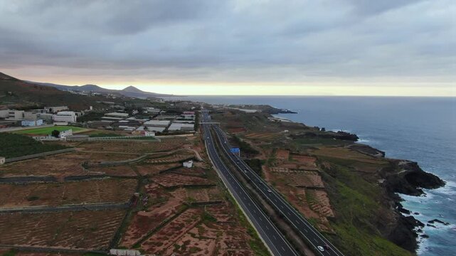 Drone view following the Northern Highway in Gran Canaria, with cars driving along the Atlantic Ocean coastline under a cloudy evening sky