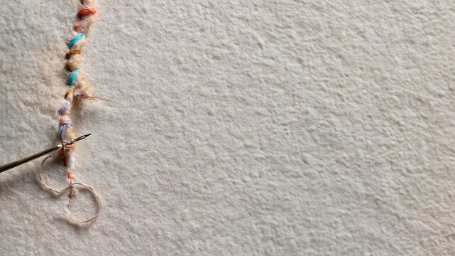 Bunte gestickte F&auml;den werden mit Nadel auf Leinenstoff kunstvoll vern&auml;ht