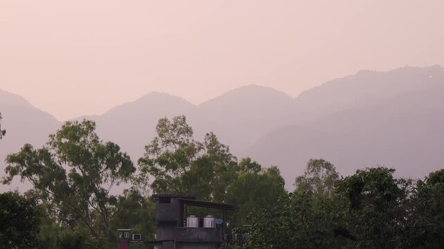 Soft evening light over the Himalayan foothills viewed from Dehradun, Kullu, Manali, Chandigarh with lush trees, residential buildings, and layered mountains creating a peaceful landscape.