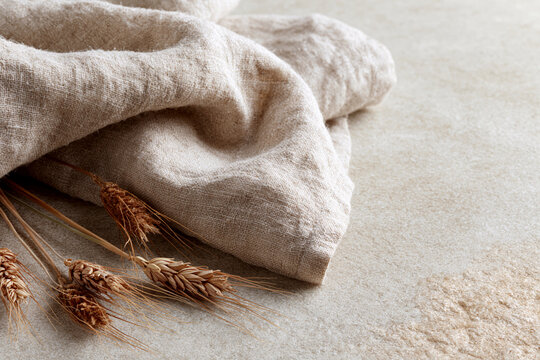 Soft linen cloth rests beside golden wheat stalks. Flour dusted surface adds rustic, natural texture. Warm tones evoke earthy, artisanal comfort. Ideal for farmhouse, kitchen, or seasonal branding