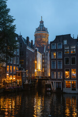 Naklejka premium Basilica of Saint Nicholas dome reflecting in an Amsterdam canal with illuminated historic houses at dusk