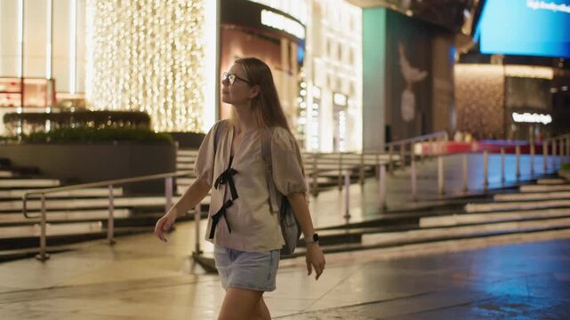 Beautiful night cityscape in Singapore as a female tourist walks past illuminated storefronts enjoying the vibrant downtown atmosphere and urban travel in Asia
