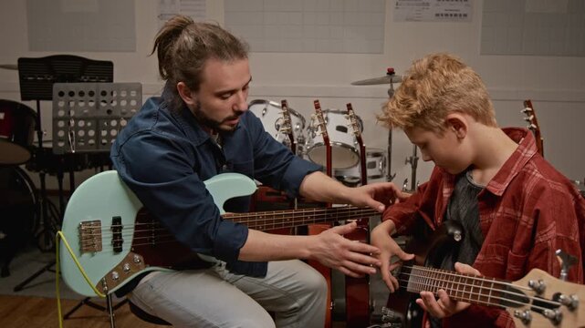 Male music teacher instructing teenage boy on playing bass guitar during private lesson. Footage for promoting music schools and creative youth education programs