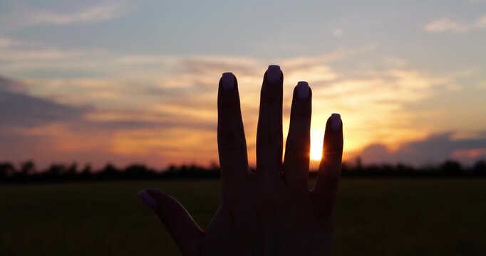 Silhouette of woman hand reaching toward glowing sunset above open field. hope, new beginnings, freedom and optimism in peaceful natural landscape during golden hour.