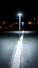 Obraz premium Streetlight illuminating a dark road at night with streetlights in background.