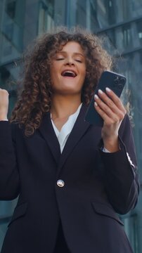 Bottom view emotional happy Caucasian business woman receive good news mobile phone message celebrating winning near skyscraper in city carefree girl businesswoman female employer win prize online
