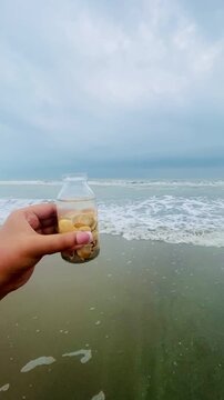 Seashells on the bottle on the seabeach. Selective focus of a small bottle in hand with tiny shells on beach sand. keep moment in little bottle. Collecting pebbles on a glass bottle. 