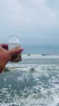 Seashells on the bottle on the seabeach. Selective focus of a small bottle in hand with tiny shells on beach sand. keep moment in little bottle. Collecting pebbles on a glass bottle. 