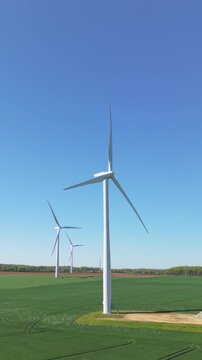 Aerial view approaching wind turbines on a wind farm generating clean and renewable energy on agricultural land with crops in fields and sunny blue sky