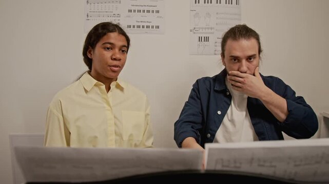 Young Caucasian male teacher and teenage African American female student discussing sheet music. Video for promoting music schools, private tutoring, or creative arts education