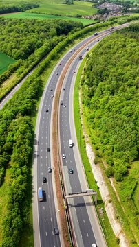 Aerial view above a busy UK motorway through British countryside with downward motion revealing traffic speeding on long distance journeys