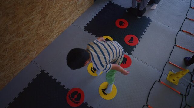 A young child engages in an agility game using colorful hand and foot markers on the floor. This interactive play session promotes kids fitness and coordination skills.
