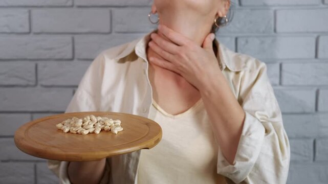 Woman with food allergy scratching her neck. Unrecognizable woman holding a plate of peanuts and scratching her red, irritated neck, showing signs of an allergic reaction, itching