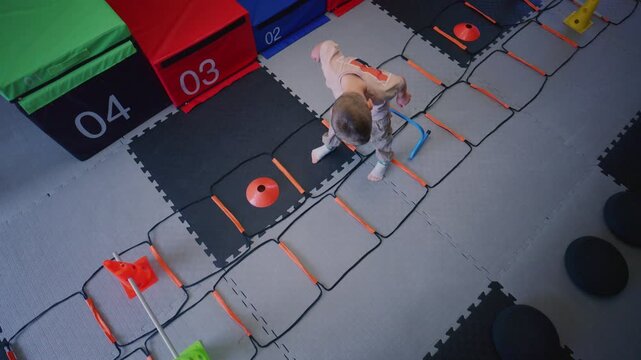 A young boy enthusiastically engages in agility ladder exercises and jumps over small hurdles indoors.