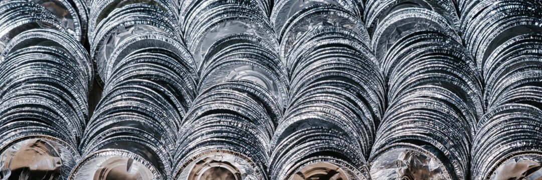 Rows of stacked aluminum foil trays. Clean metal containers ready for food packaging. Recycling and waste management theme. Industrial manufacturing and environmental sustainability concept.