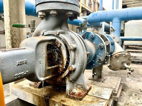 Close-up of a damaged centrifugal water pump with leaking seal and splashing water in an industrial plant, illustrating equipment failure, maintenance, repair, reliability and mechanical engineering.