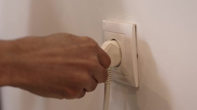 Close-up of a hand plugging an electrical appliance into an EU wall power outlet, illustrating electricity use, home energy, and connecting a power cord
