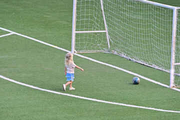 Fototapeta premium unrecognizable blonde female child playing alone on soccer football pitch