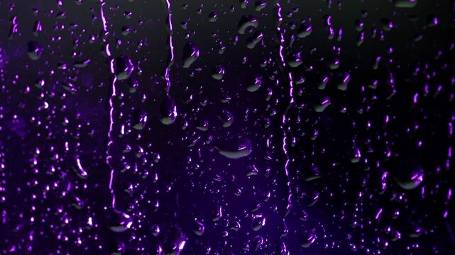 View of glass with raindrops during a thunderstorm, wet glass is purple