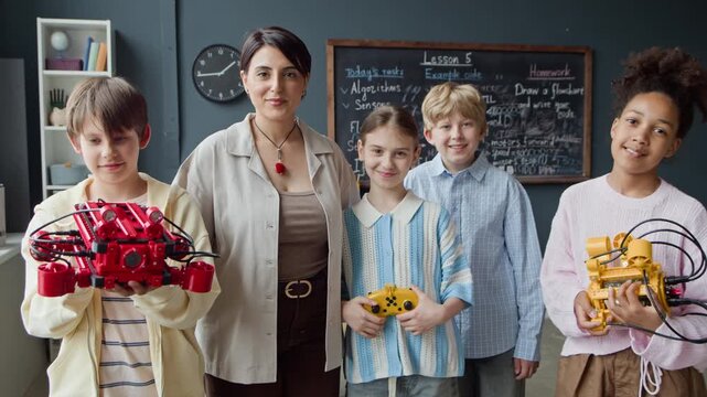 Portrait of female teacher and multiethnic kids holding handmade robots and controllers in classroom. Video is ideal for promoting STEM education programs and modern school curricula