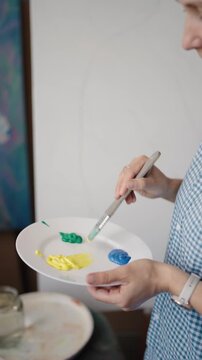 Close up view of a woman artist mixing acrylic paints on a white palette with a brush. Creative process of a painter working on a new masterpiece in an art studio, inspiration and hobby. vertical