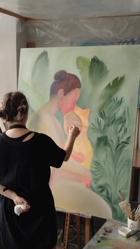 Talented woman painter creating a large, colorful oil painting on canvas in her art studio, applying precise brushstrokes to a figurative artwork. This reveals her creativity and dedication. vertical