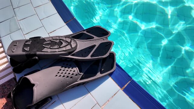 Black fins lie by the pool ready for a swim on a sunny day.