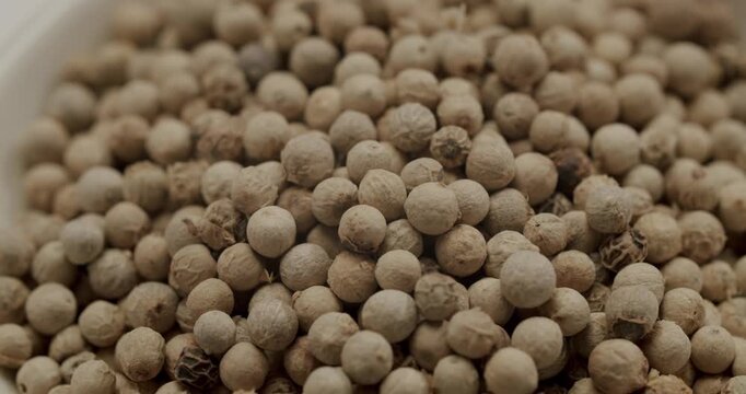 White peppercorns rotating in a detailed macro shot, showcasing the texture and aroma of the popular culinary spice used for seasoning and flavoring in various dishes worldwide
