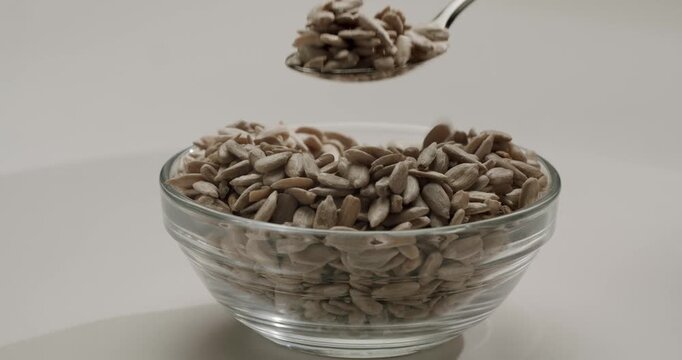 Spoon scooping organic sunflower seeds from a transparent glass bowl isolated on a white background, highlighting a healthy, natural, and nutritious ingredient for vegetarian and vegan diets
